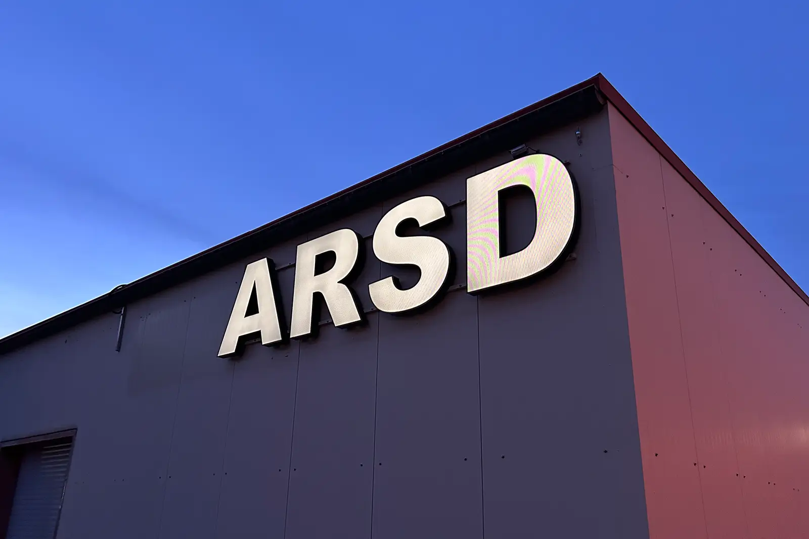 Weiß leuchtende Profilbuchstaben ARSD unter der Dachkante einer Gewerbehalle